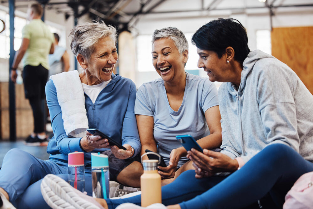 Gym, smartphone and senior women laughing at meme on phone after fitness class, conversation