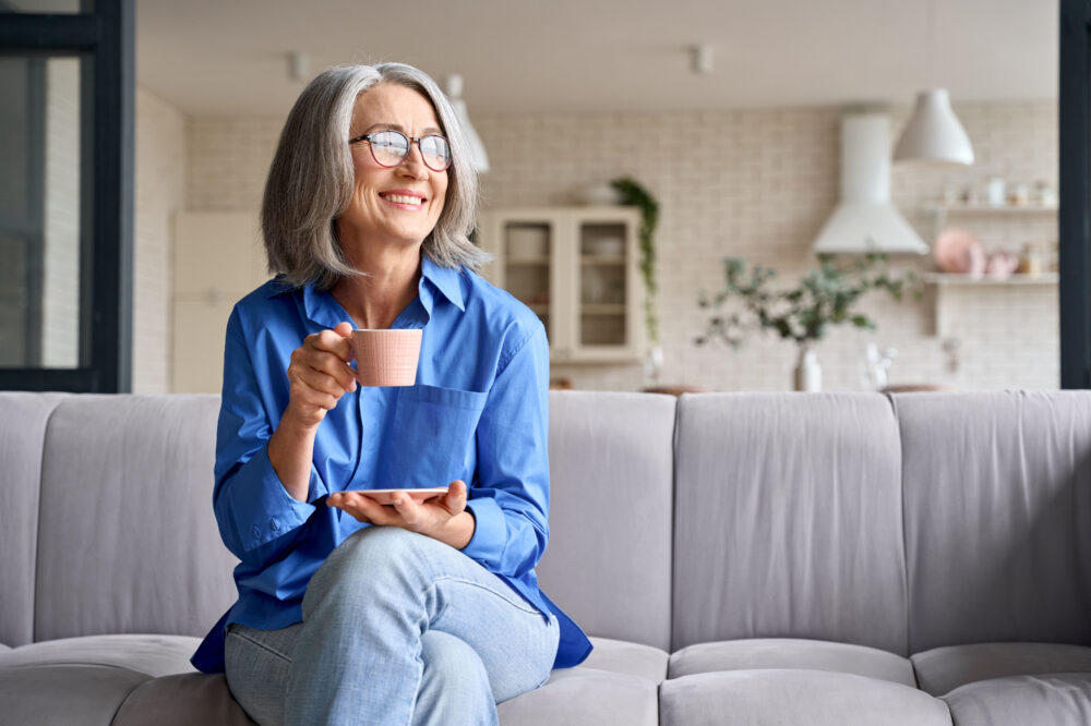 Senior smiling woman sitting on the sofa and drinking tea