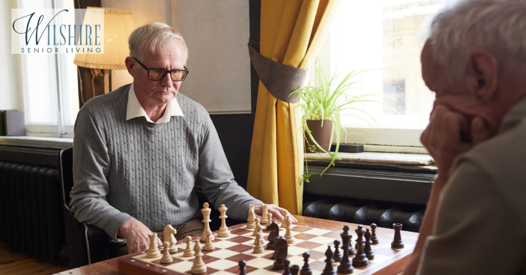 Two elderly men are playing chess, a stimulating memory care activity idea that promotes critical thinking, memory retention, and social interaction among seniors.