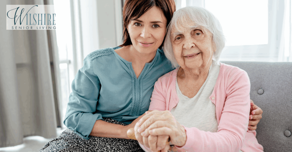 An elderly woman smiling while holding hands with her supportive daughter, symbolizing love, connection, and compassionate Alzheimer’s care at home.